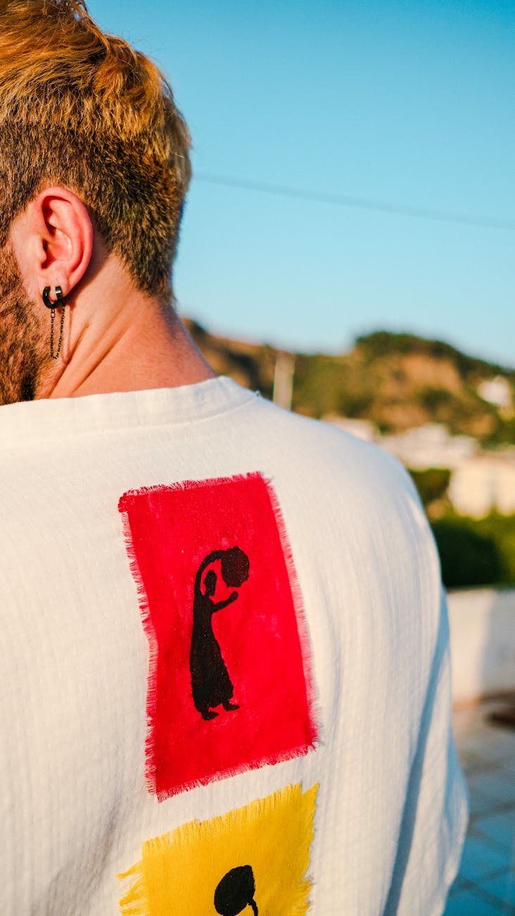 A man with dyed short hair is wearing a shirt with artistic prints, outdoors.